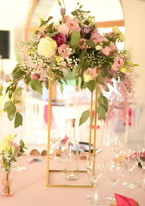Centre de table haut sur colonne dorée : roses, œillets roses, lisianthus et gypsophile retombante, réalisé par Mily Fleurs